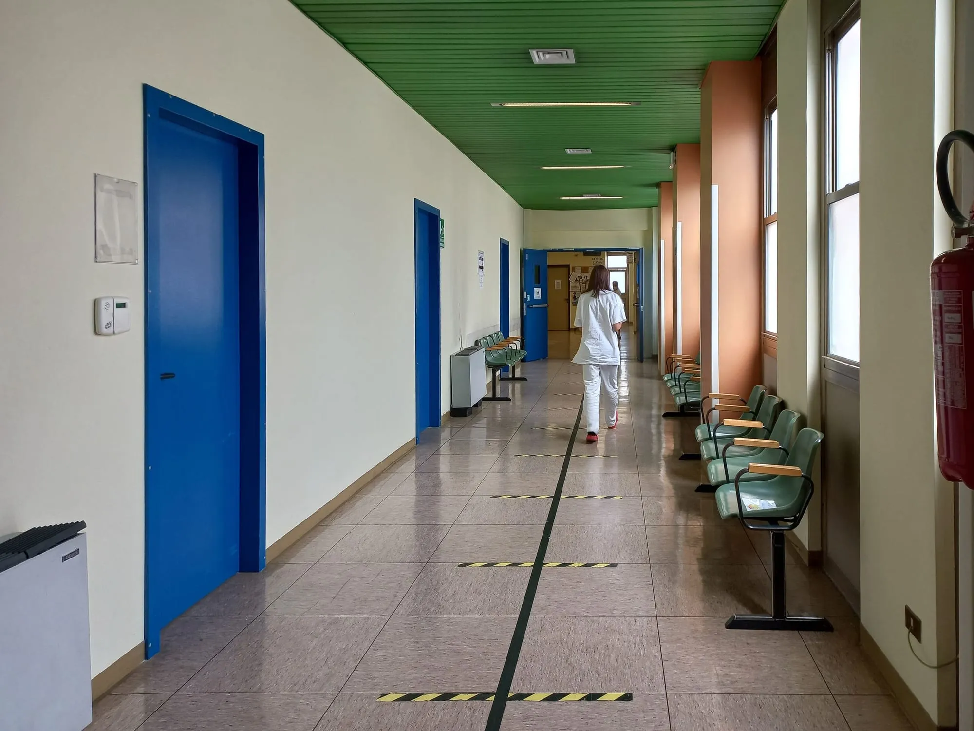 Soignante en blouse blanche marchant de dos dans un couloir d’hôpital